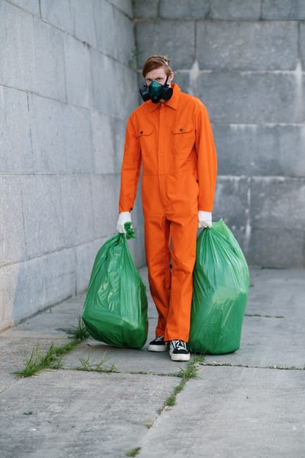 A pile of bulky waste cluttering a small outdoor area adjacent to a brick wall, including wooden pallets leaning against each other, a shattered white plastic object, and various discarded materials s