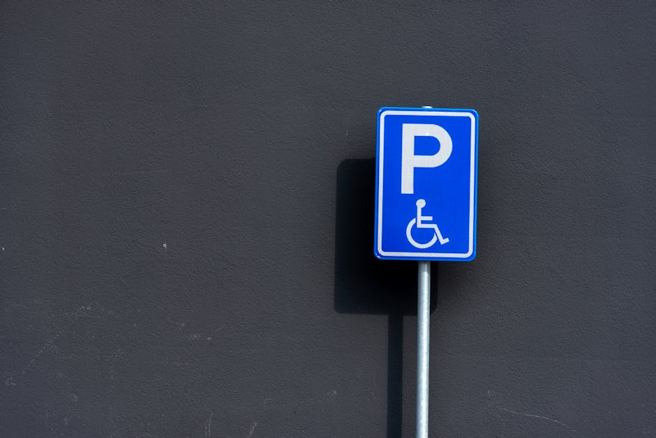 Close-up view of an asphalt parking lot surface with clearly visible yellow painted markings for accessible parking spaces. The markings include the international symbol of access, a wheelchair icon,